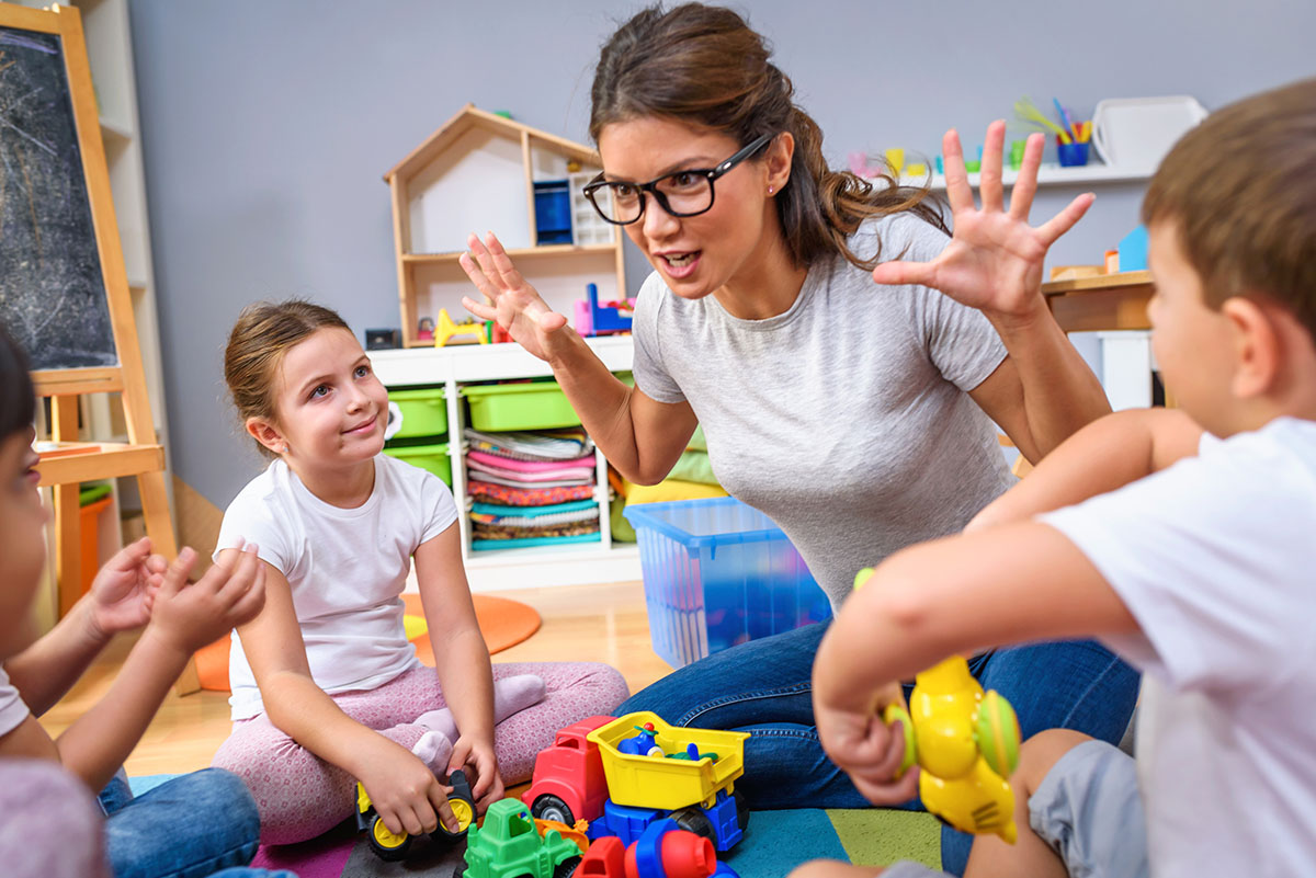 Preschool teacher talking to group of children sitting on a floor at kindergarten